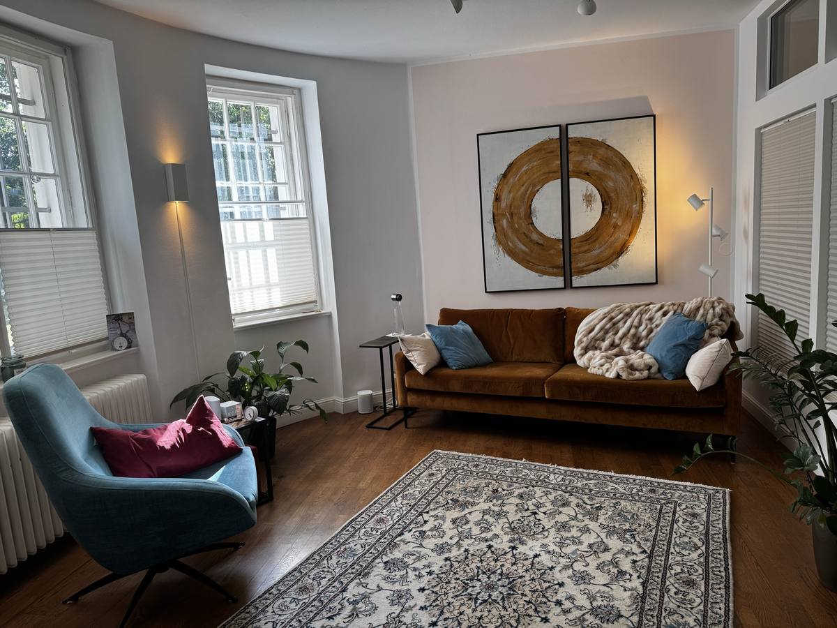 Der wohnliche Behandlungsraum von Jenny Völker mit Cognac-Samtsofa, Holz, Pflanzen und warmem Tageslicht